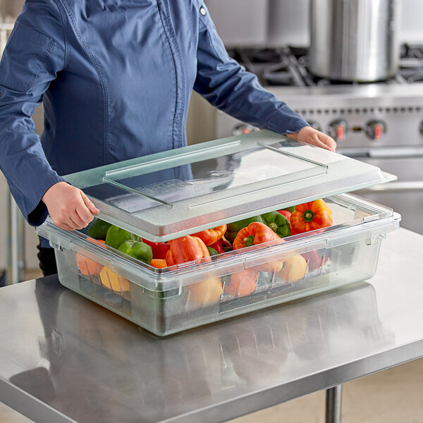 A woman in a chef's uniform holding a Carlisle green food storage box filled with vegetables.