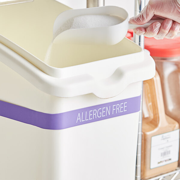 A person in plastic gloves using a Baker's Mark silicone band to pour sugar into a white container.