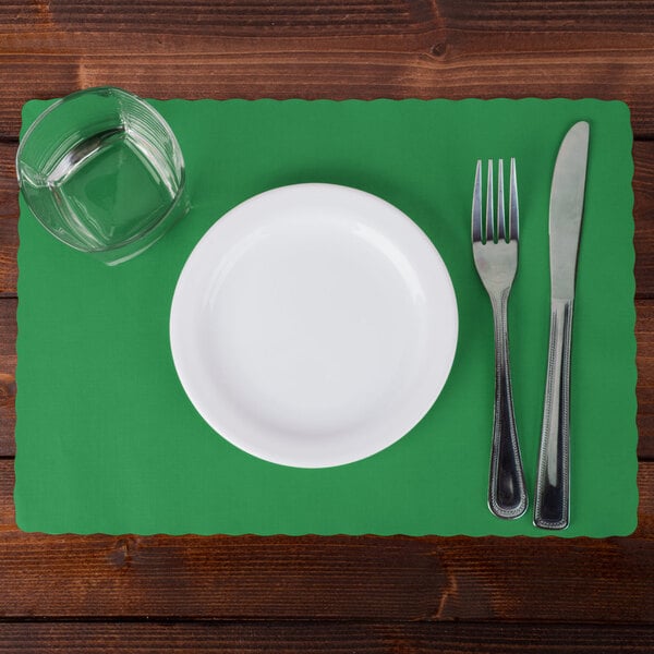 A white plate with a fork and knife on a jade green scalloped paper placemat.
