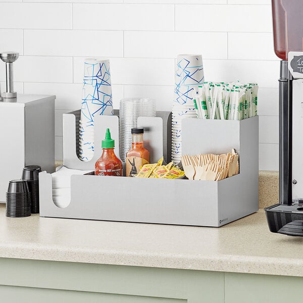 A ServSense stainless steel countertop sectioned organizer with condiments and cups inside.