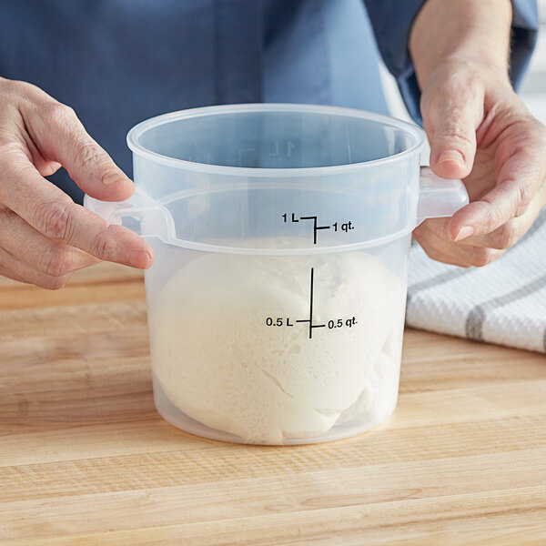 A person holding a measuring cup with a ball of white dough in it.