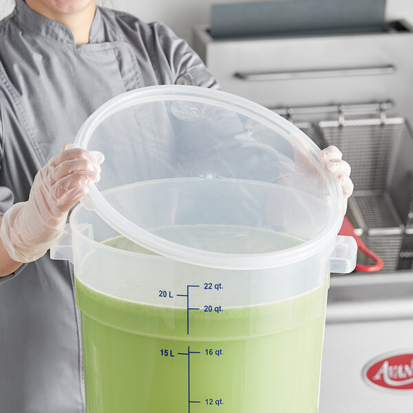 A woman holding a Vigor translucent round polypropylene food storage container lid filled with green liquid.