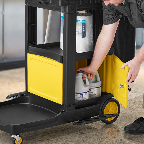 A man using a Lavex yellow lock box on a janitor cart with bottles of liquid.