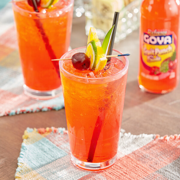 A glass of Goya fruit punch soda with ice and a straw.