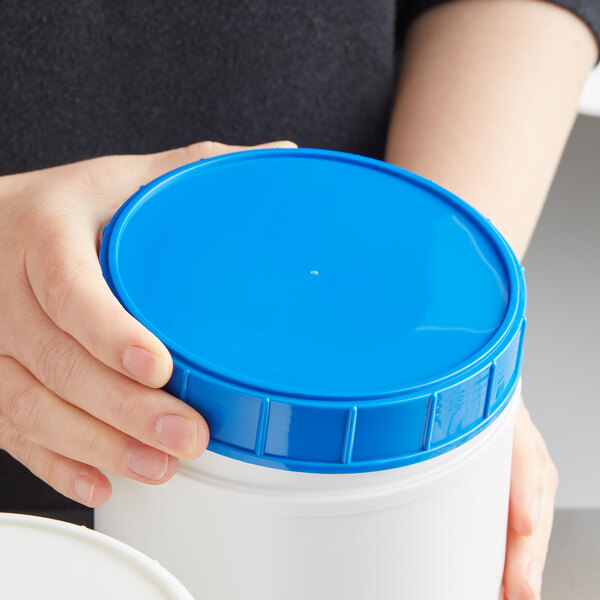 A person holding a blue plastic canister lid.