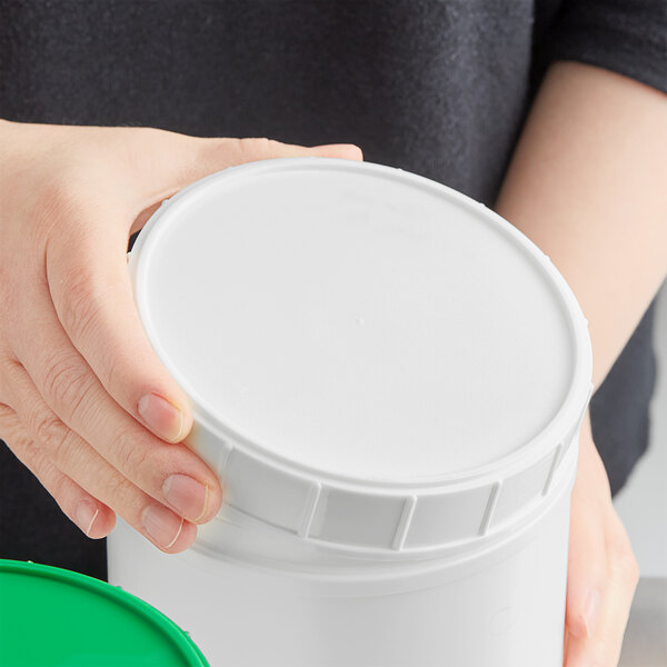 A person holding a white 120 mm plastic canister lid.