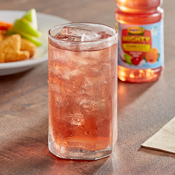 A glass of Mott's Mighty Flying Fruit Punch with ice on a table with a plate of food.