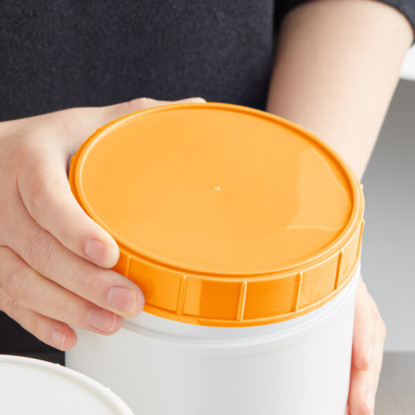 A person holding an orange plastic canister lid.