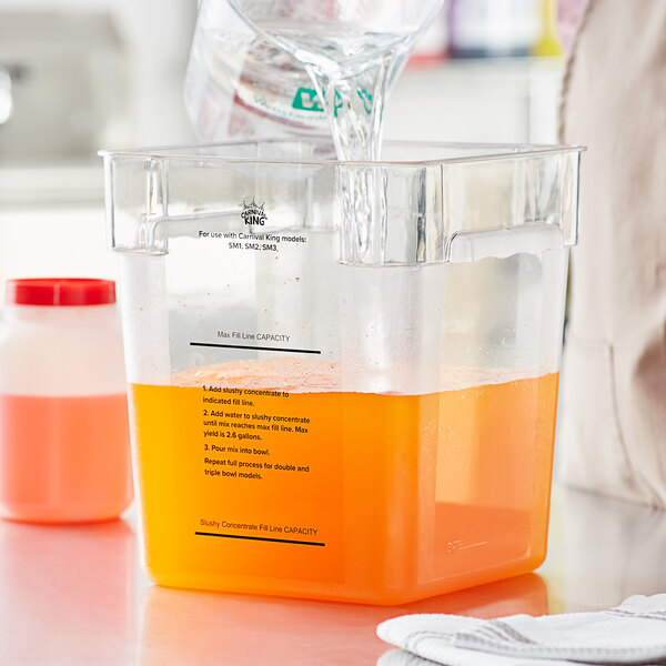 A person pouring orange liquid from a measuring cup into a clear container.