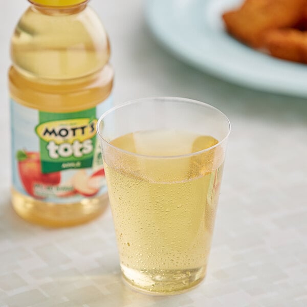 A glass of apple juice next to a bottle of Mott's For Tots Apple Juice.