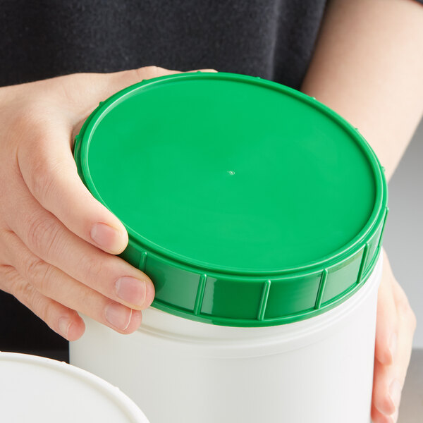 A person holding a white container with a green plastic lid.