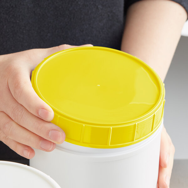 A person holding a white container with a yellow lid.