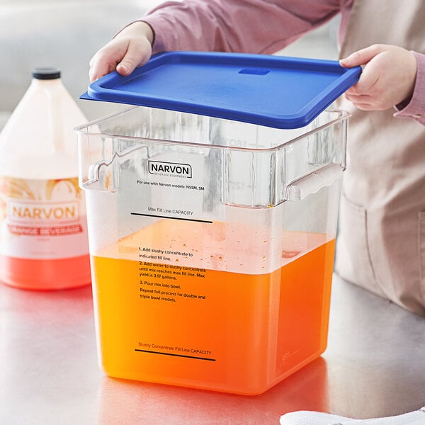 A person holding a blue lid over a container of orange liquid.