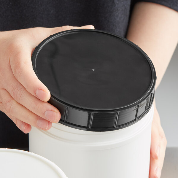 A person holding a black 120 mm plastic lid.