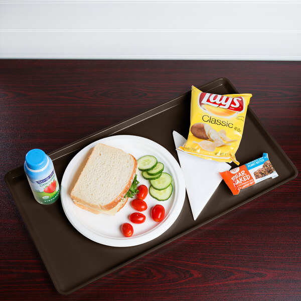 A Brazil brown Cambro dietary tray with food including a sandwich, chips, and a drink on it.