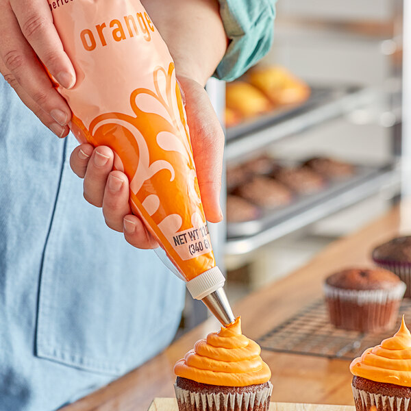 A person using Rich's Bettercreme Orange Whipped Icing from a pastry bag to frost a cupcake.