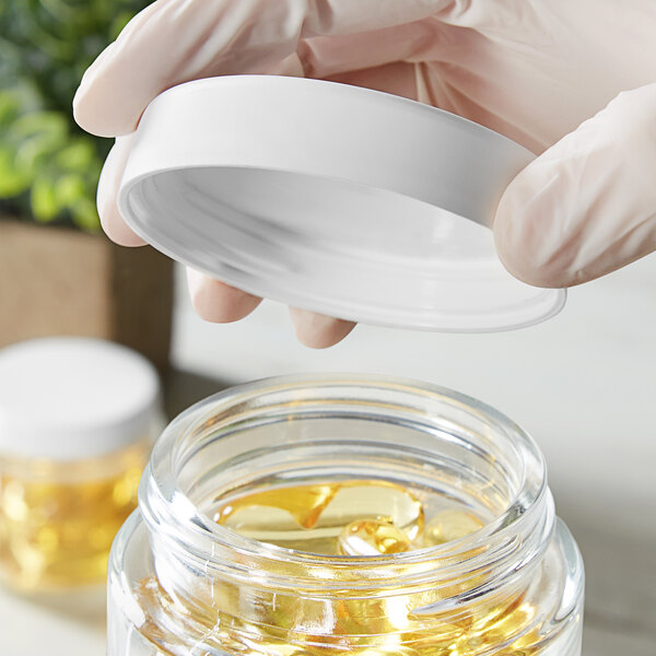 A person holding a white Child-Resistant cap over a clear jar with yellow liquid.