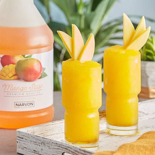 A table with two glasses of yellow Narvon Mango Slushy with fruit on the rim.