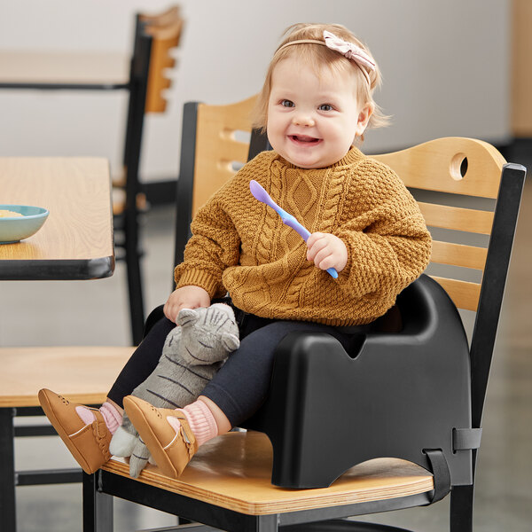 A baby sitting in a Carlisle black booster seat holding a spoon.