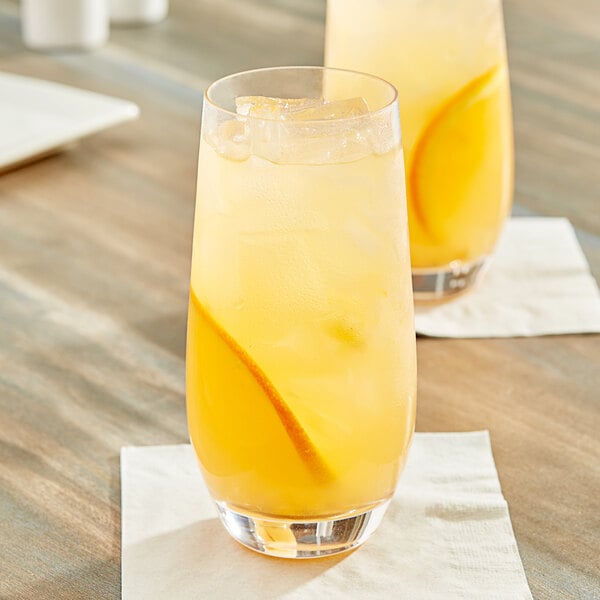 A glass of Pure Craft Beverages Orange Passionfruit beverage with ice and a slice of orange on a table.