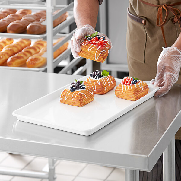 A person in a white apron holding a MFG Tray white fiberglass market display tray of pastries.