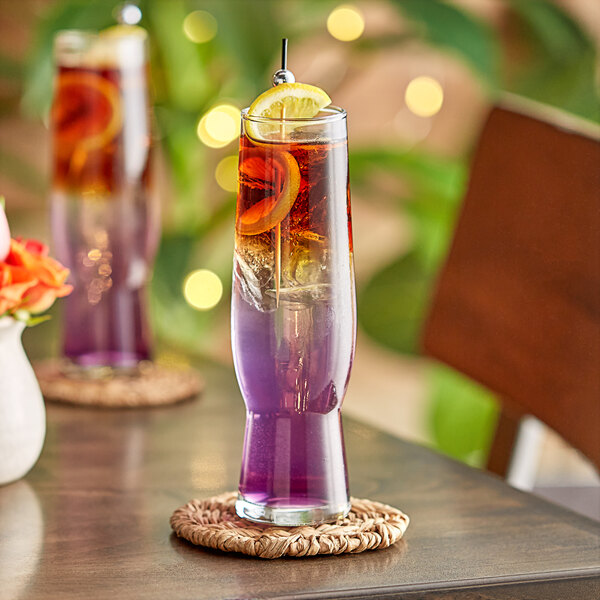 A Libbey flute glass filled with colorful purple liquid and a lemon slice on a coaster.