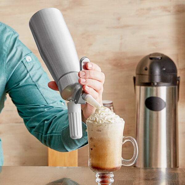 A person pouring whipped cream from a Chef Master whipped cream dispenser onto a drink.