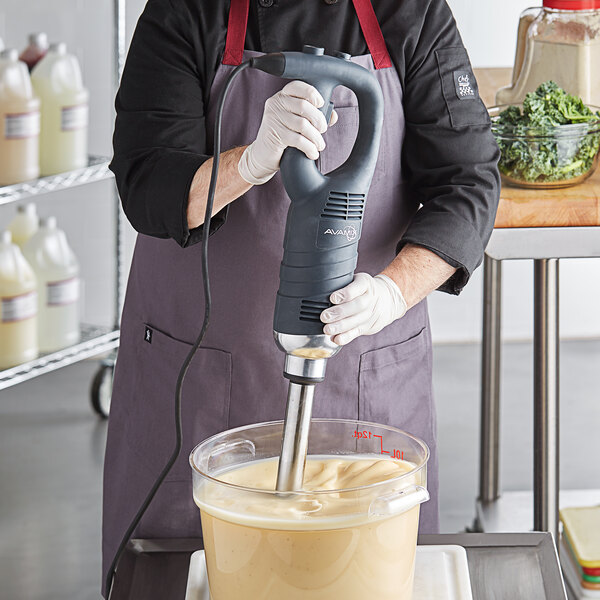 A man using a AvaMix medium-duty immersion blender on a counter in a professional kitchen.