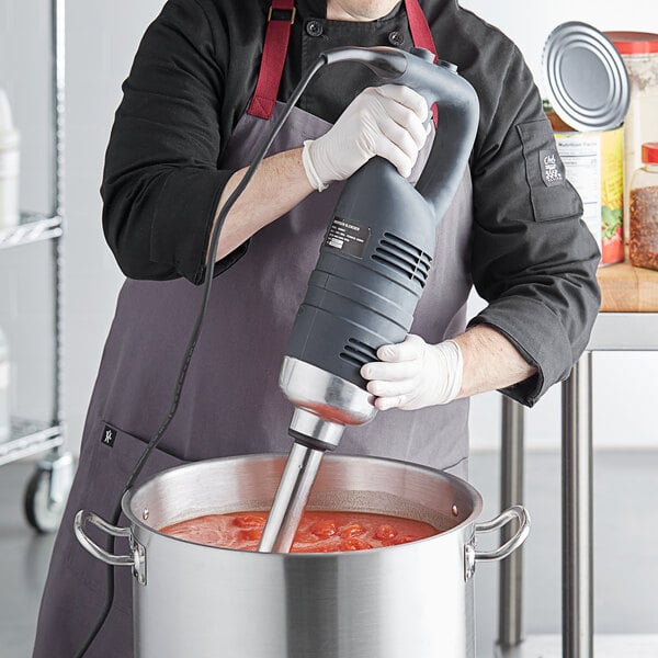 A man using an AvaMix heavy-duty immersion blender to make tomato sauce in a professional kitchen.