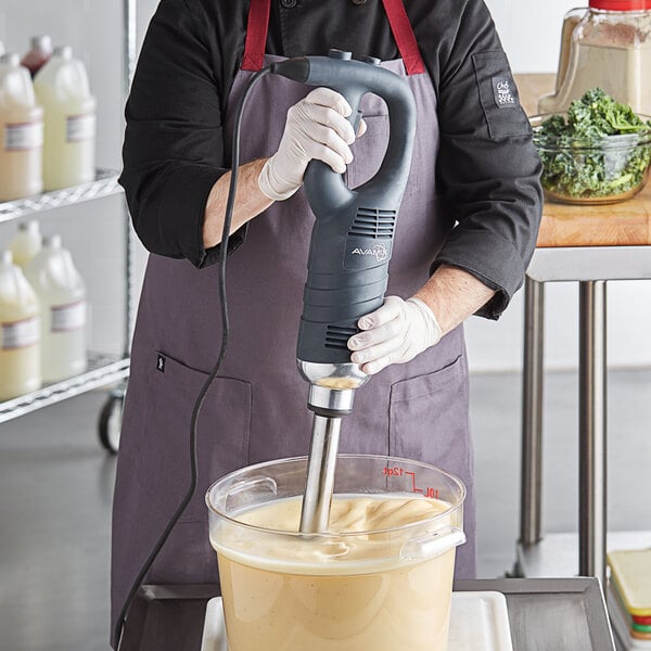 A man in a chef's hat using an AvaMix medium-duty immersion blender on a counter in a professional kitchen.