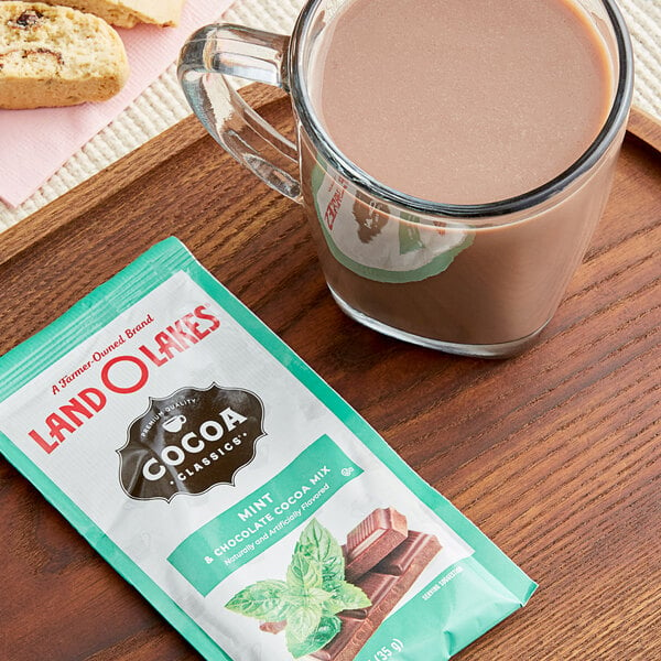 A glass mug of hot chocolate next to a packet of Land O Lakes Mint and Chocolate Cocoa Mix.