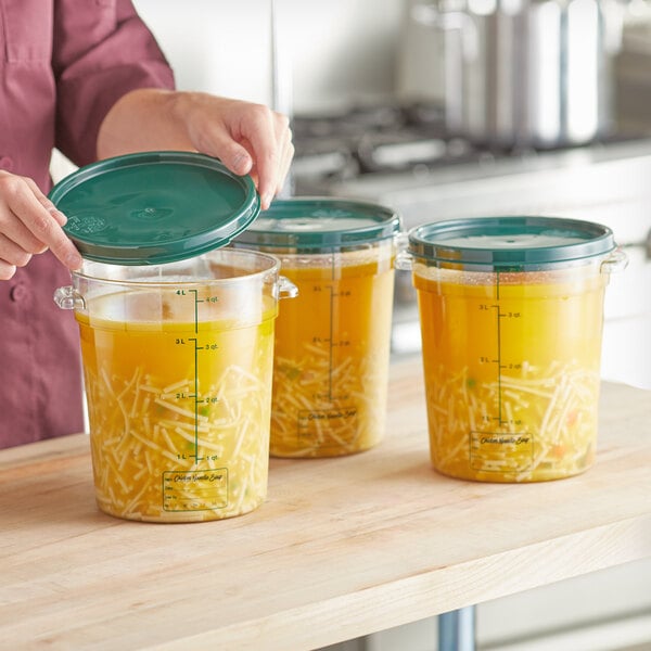 A woman opening a green plastic lid on a clear container of broth.