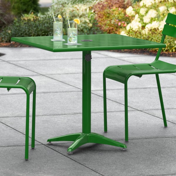 A Lancaster Table & Seating green powder-coated aluminum table with two chairs on a patio.