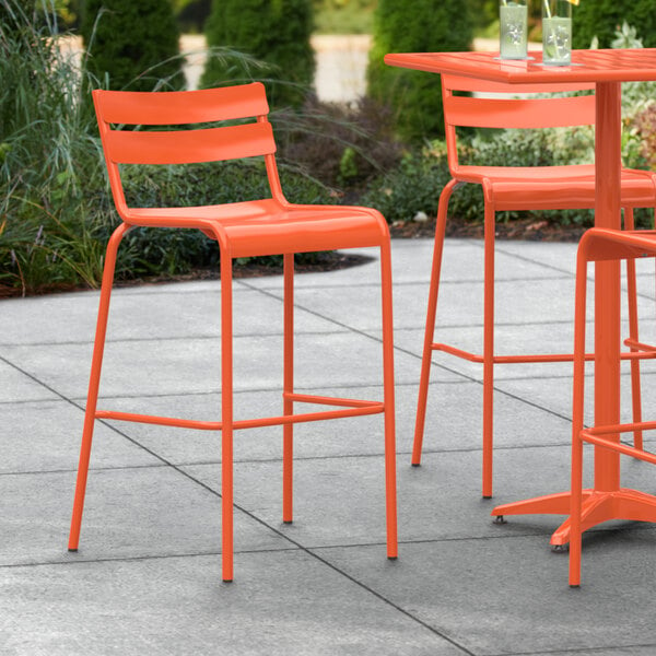 A Lancaster Table & Seating orange powder coated aluminum outdoor bar stool on a patio.