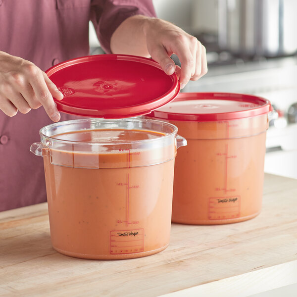 A person holding a red lid over a clear round food storage container.