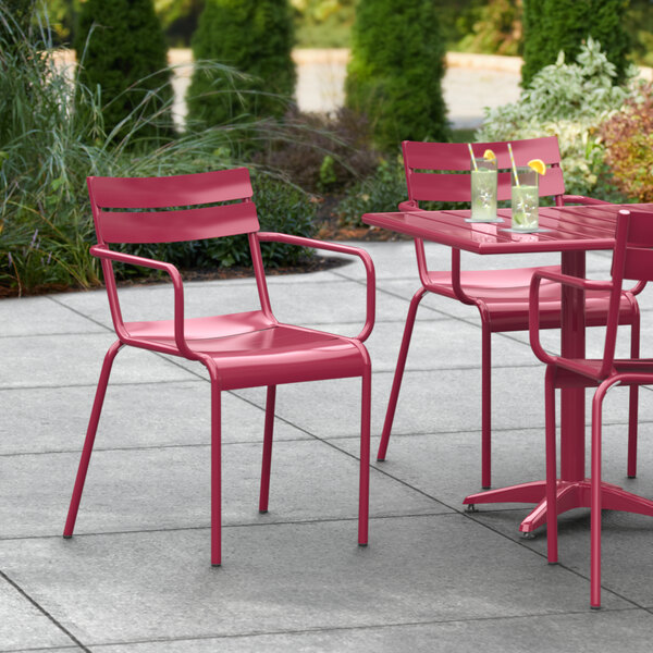 A Lancaster Table & Seating red powder coated aluminum outdoor arm chair at a table on an outdoor patio with drinks.