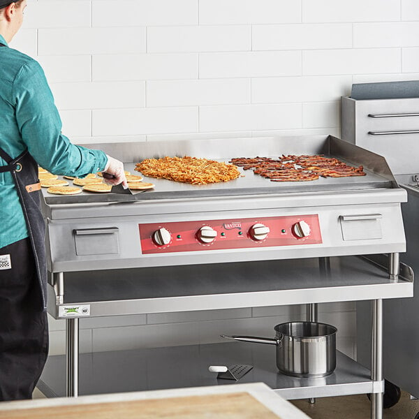 A person cooking food on a large Avantco countertop electric griddle.