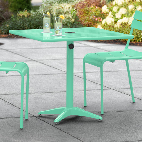 A Lancaster Table & Seating sea foam green outdoor table with umbrella hole on a patio.
