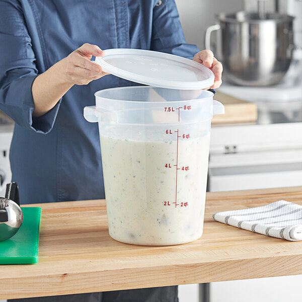 A woman pouring white liquid from a measuring cup into a Vigor translucent food storage container with a translucent lid.