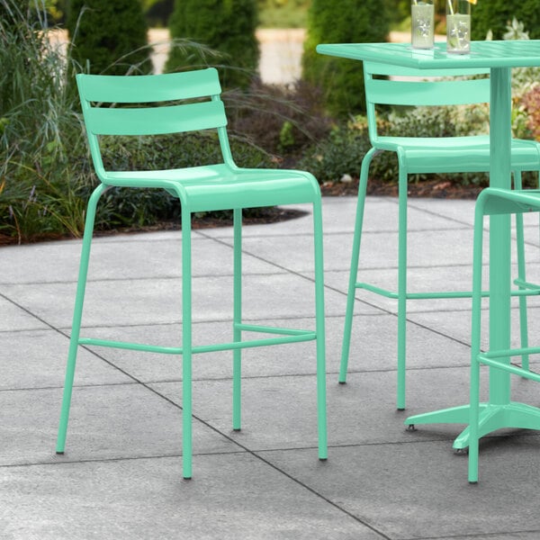 A set of three Lancaster Table & Seating sea foam green bar stools on a patio.