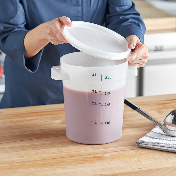 A woman pouring pink liquid into a white Vigor food storage container with a white lid.