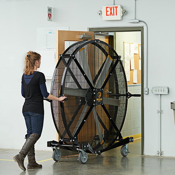 A woman pushing a Big Ass Fans Black Jack portable floor fan.