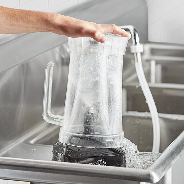 A hand pouring water from a container into a blender jar on a counter.