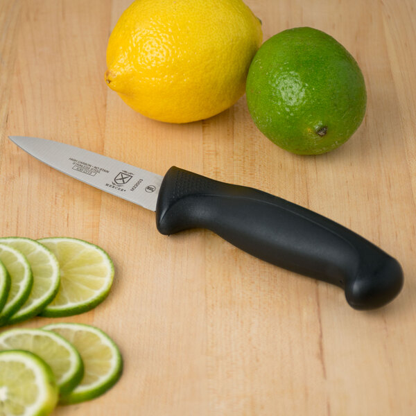A Mercer Culinary Millennia paring knife with a black handle next to a lime and sliced lemons.