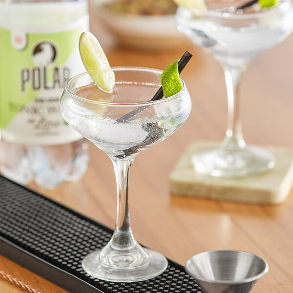 A martini glass of clear liquid with a lime slice on top of it and a bottle of Polar Diet Lime Tonic Water.