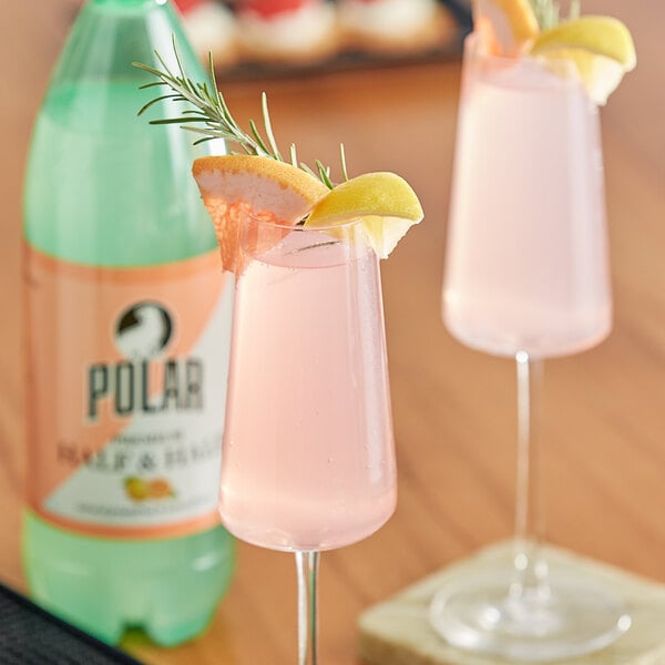 Two glasses of pink Polar sparkling citrus mixer with orange slices and a sprig of rosemary on a table.