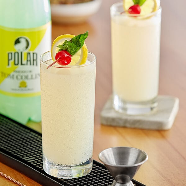A bottle of Polar Tom Collins Sparkling Citrus Mixer on a table with a glass of white liquid with a lemon slice, cherry, and leaf.