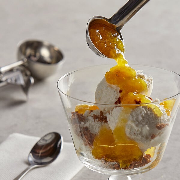A spoon pouring I. Rice pineapple dessert topping onto a glass of ice cream.