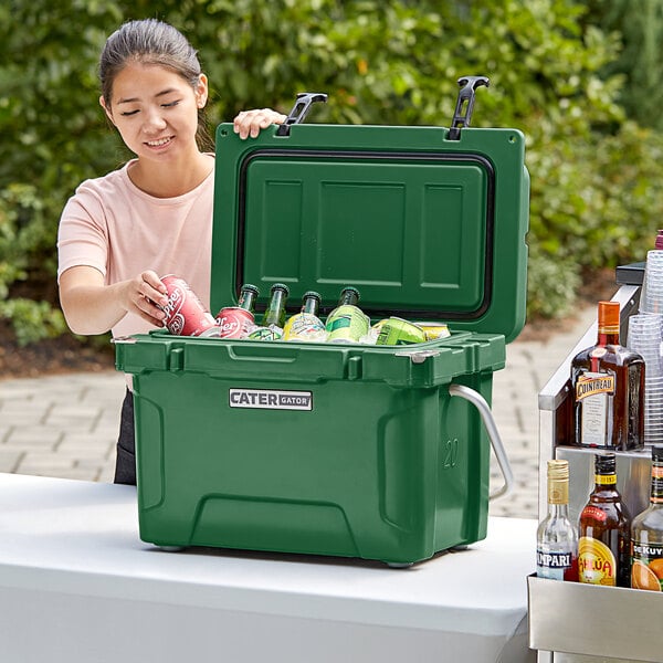 A woman opening a CaterGator Hunter Green cooler to put in bottles and cans of soda.