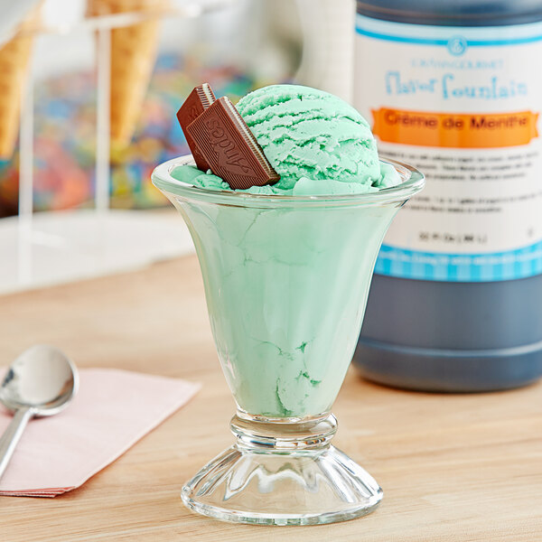 A glass bowl of green ice cream with a chocolate bar on top.